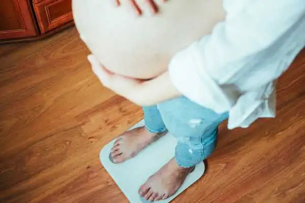 Image of woman weighing herself and experiencing weight gain through pregnancy Windlesham